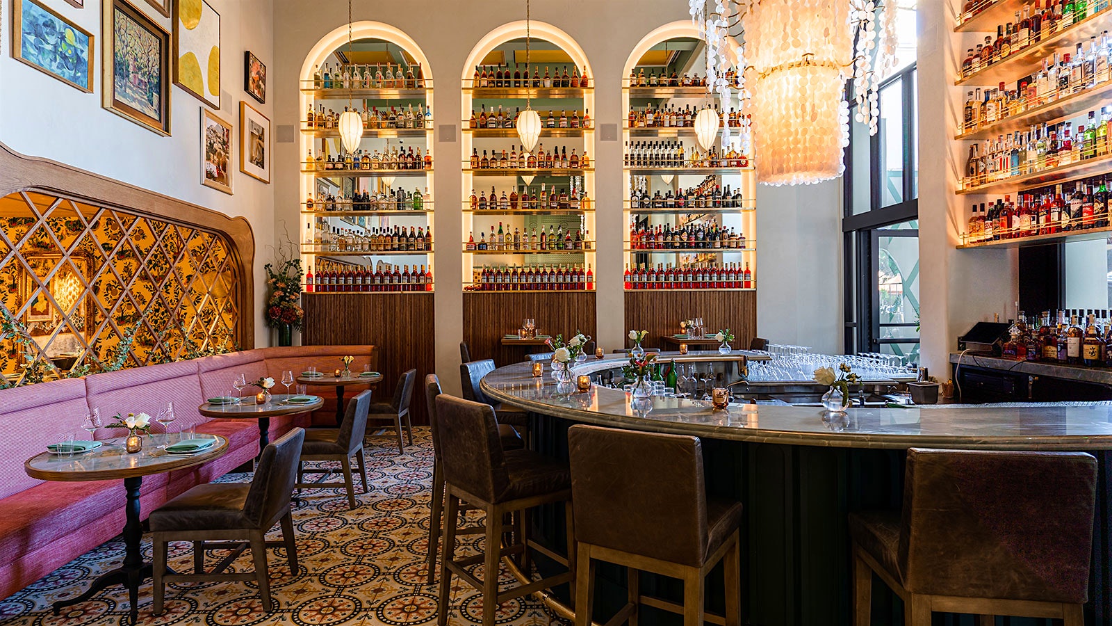  El área del bar de Marisi cuenta con una barra en forma de media luna, banquetas color granate e inserciones de pared arqueadas con estantes para licores y botellas de vino.